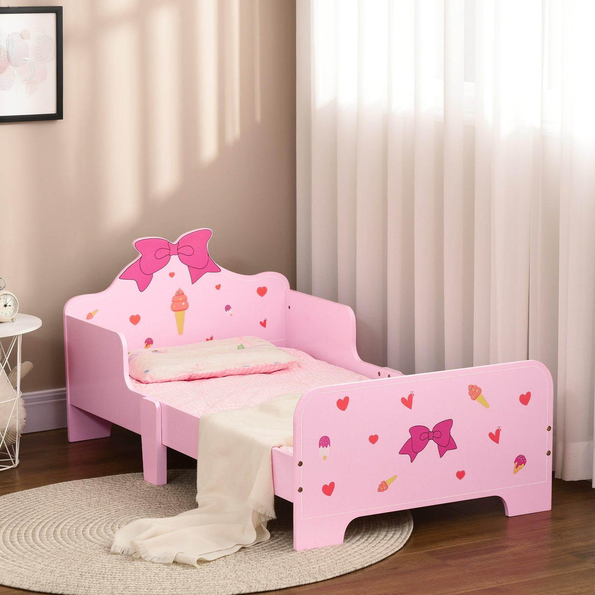 Pink toddler bed with heart and bow pattern side rails in a bedroom setting