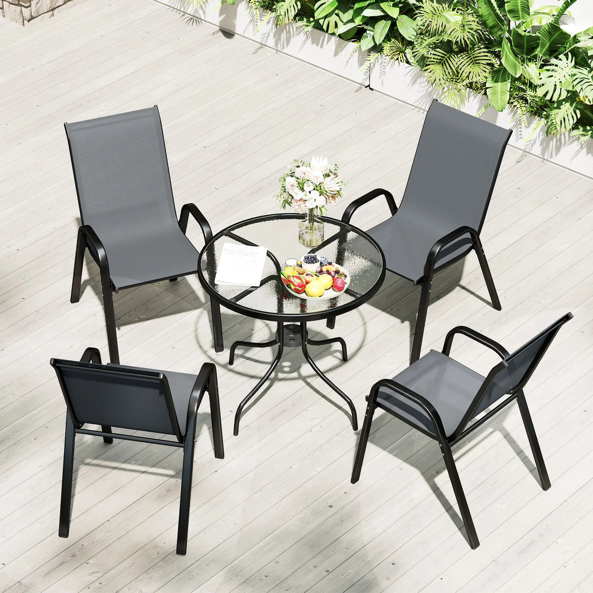 Outdoor arrangement with round glass-top table and four dark grey stackable patio chairs
