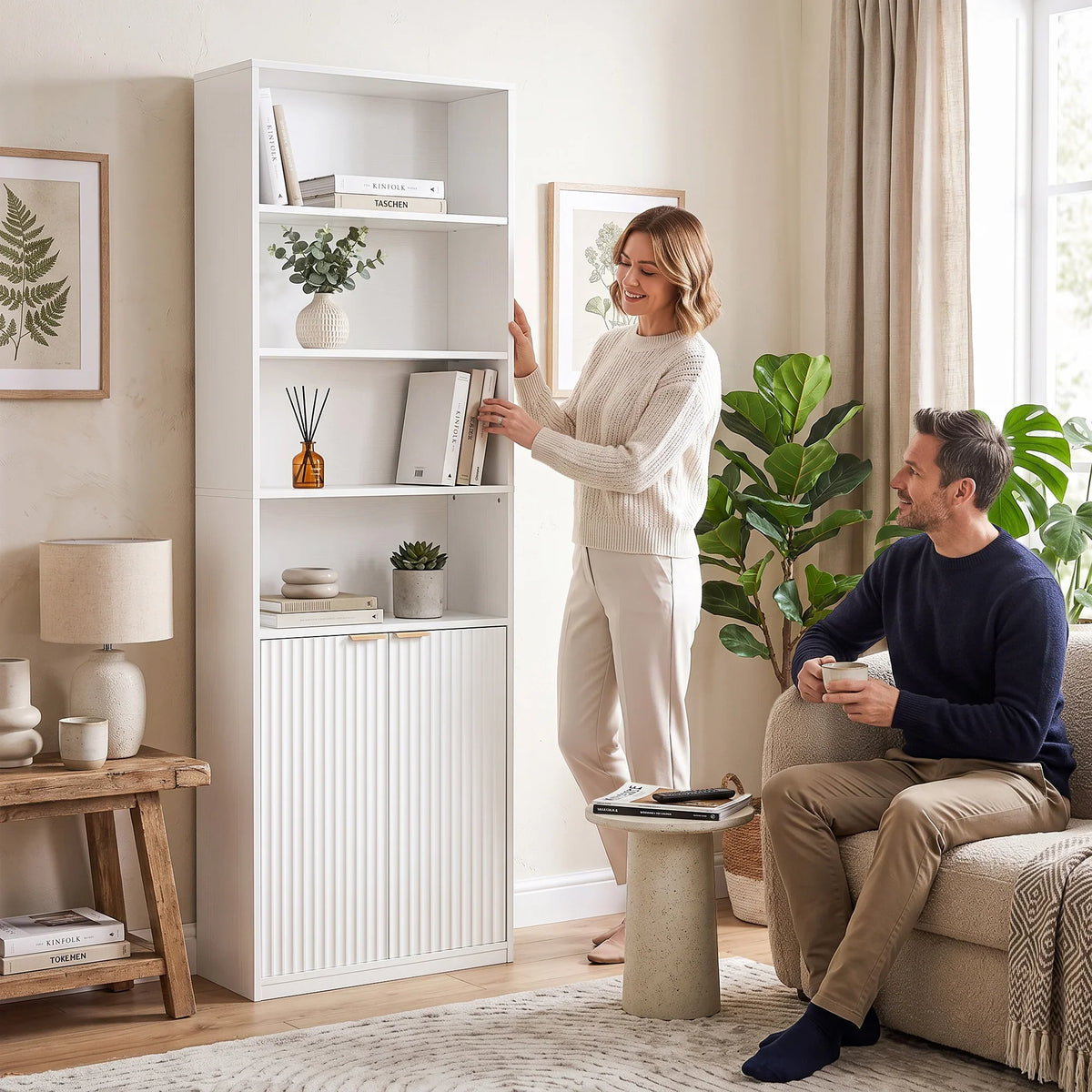 White tall bookcase with open shelves and double doors, person arranging items inside.
