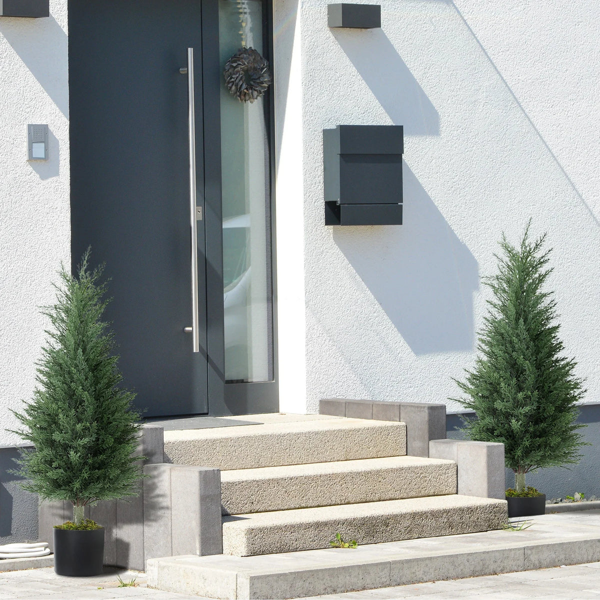 Pair of artificial cypress trees with green faux branches in black pots near entrance