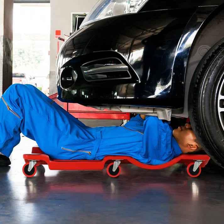Mechanic using red rolling creeper under black car in garage
