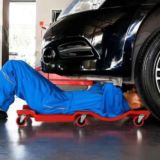 Mechanic using red rolling creeper under black car in garage