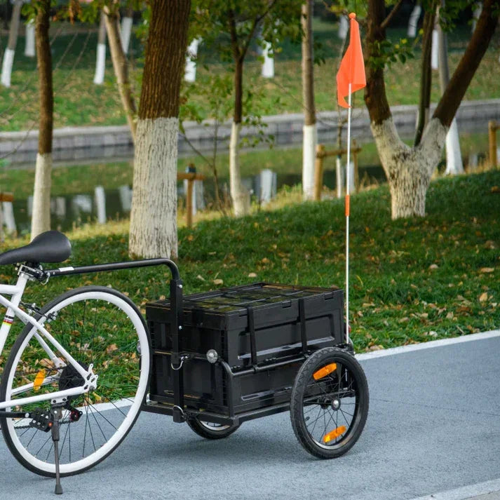 Black bike cargo trailer with orange safety flag, attached to white bicycle on park path