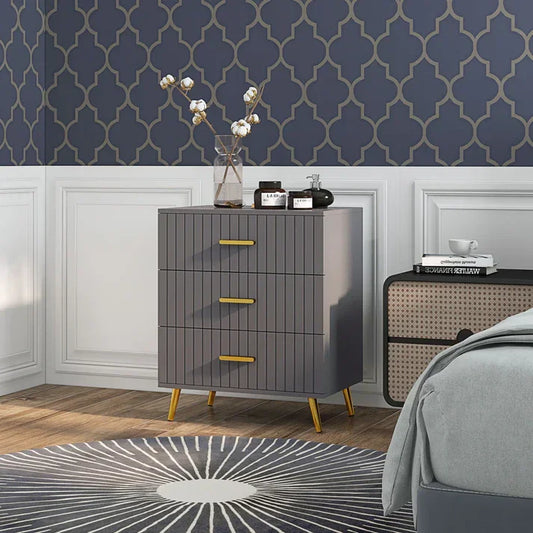 Modern gray 3-drawer nightstand with gold handles, styled in bedroom with patterned wallpaper and rug