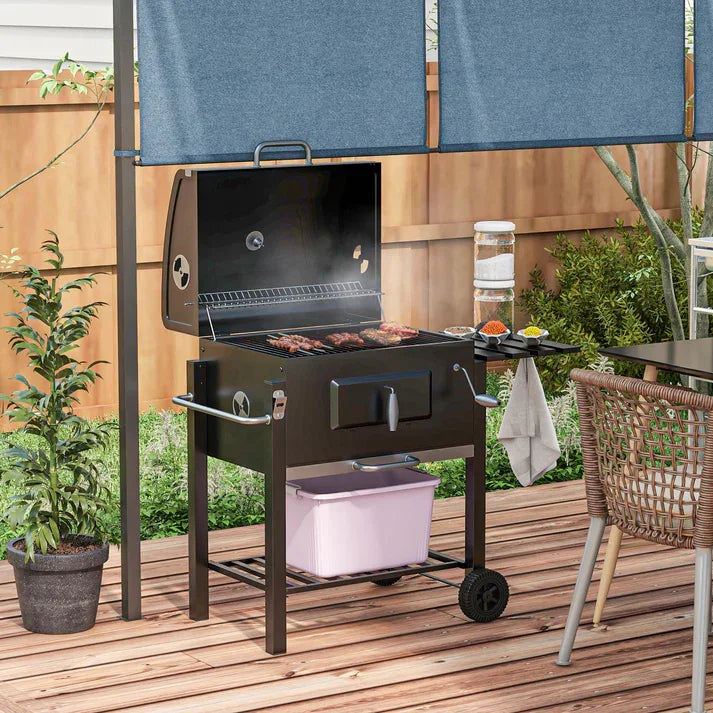 Black outdoor charcoal grill with wheels, grilling steaks on wooden deck, perfect for backyard BBQs and garden gatherings