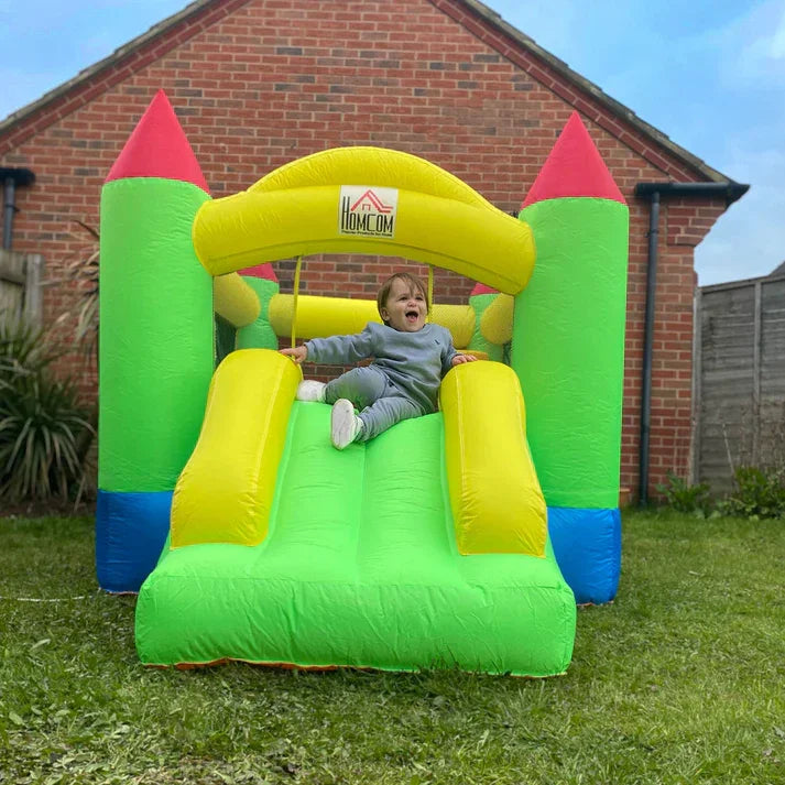 Child sliding down colorful inflatable bounce house with slide in backyard garden