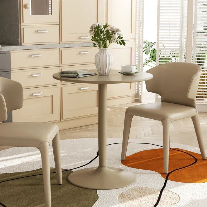Modern round dining table with beige chairs, vase of flowers, and stylish rug in bright kitchen setting