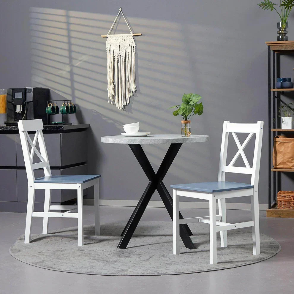 Modern round dining table with black X-legs and two white chairs with blue seats in cozy home setting