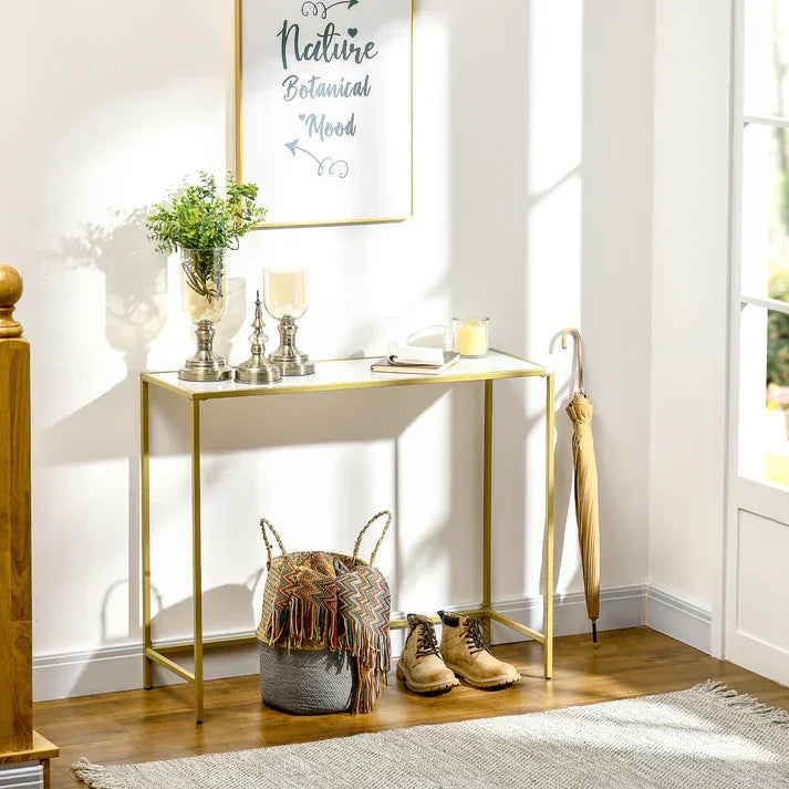 Gold metal console table with glass top, styled with plants, candles, and decor in bright entryway