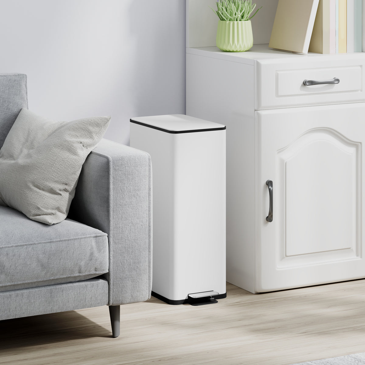 White slim pedal trash bin beside a sofa and cabinet, black base and foot pedal
