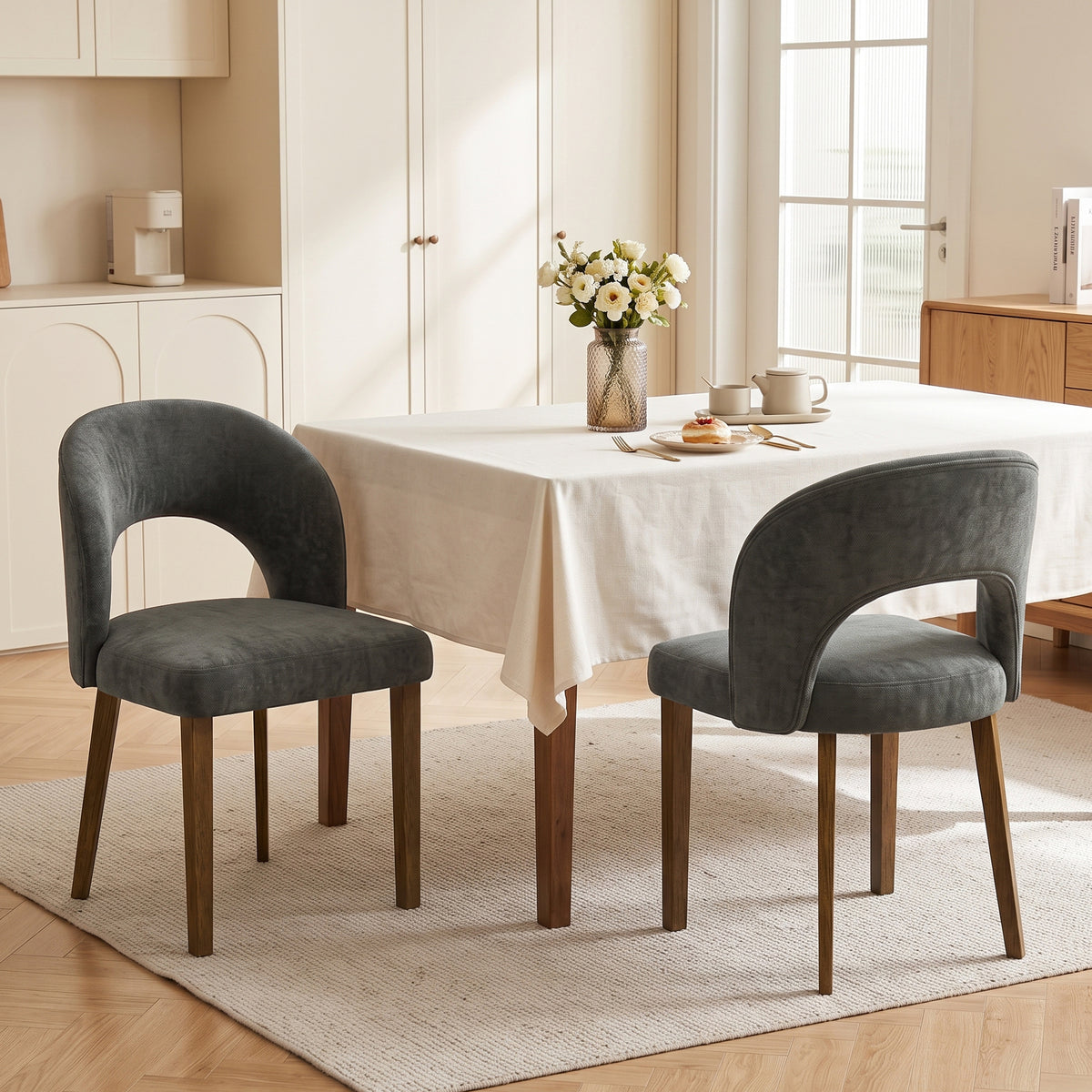 Two dark grey upholstered dining chairs with arched backs and wooden legs