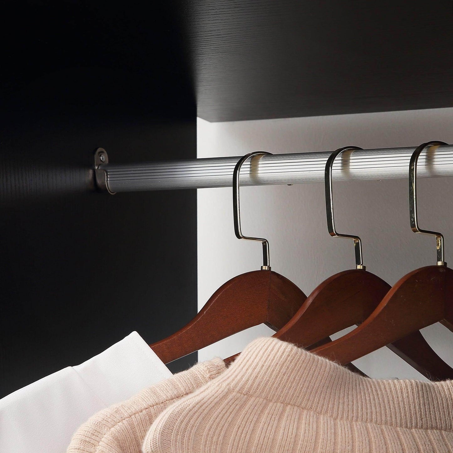 Black double open wardrobe with silver hanging rails and wooden hangers holding beige knitwear and white shirt