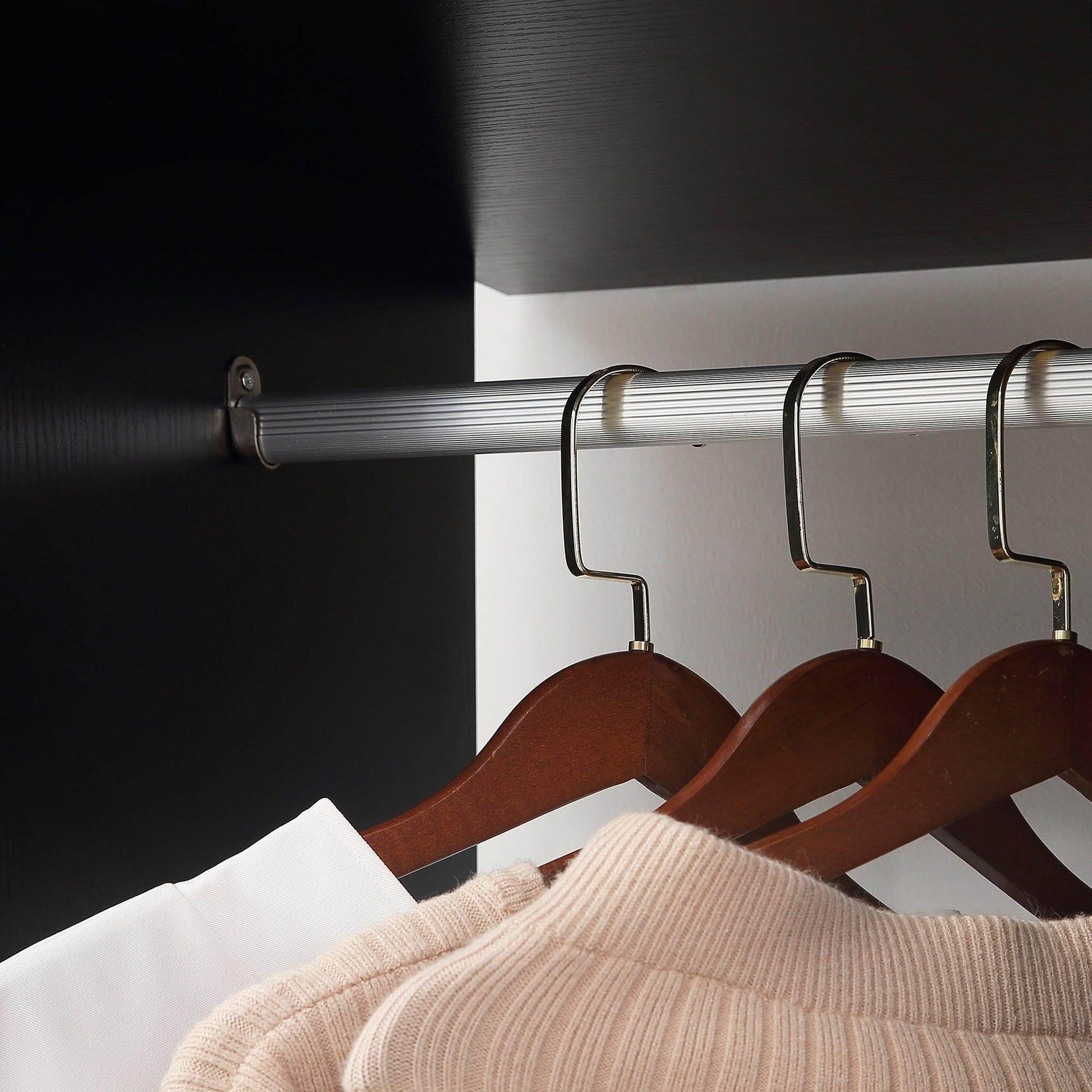 Black double open wardrobe with silver hanging rails and wooden hangers holding beige knitwear and white shirt