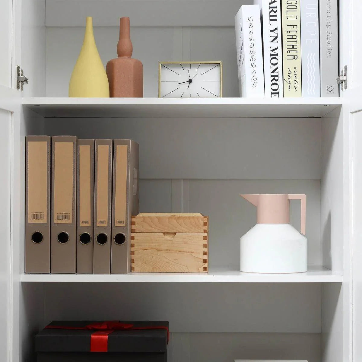 Interior of white cabinet showing shelves with binders and decorative vases, door open