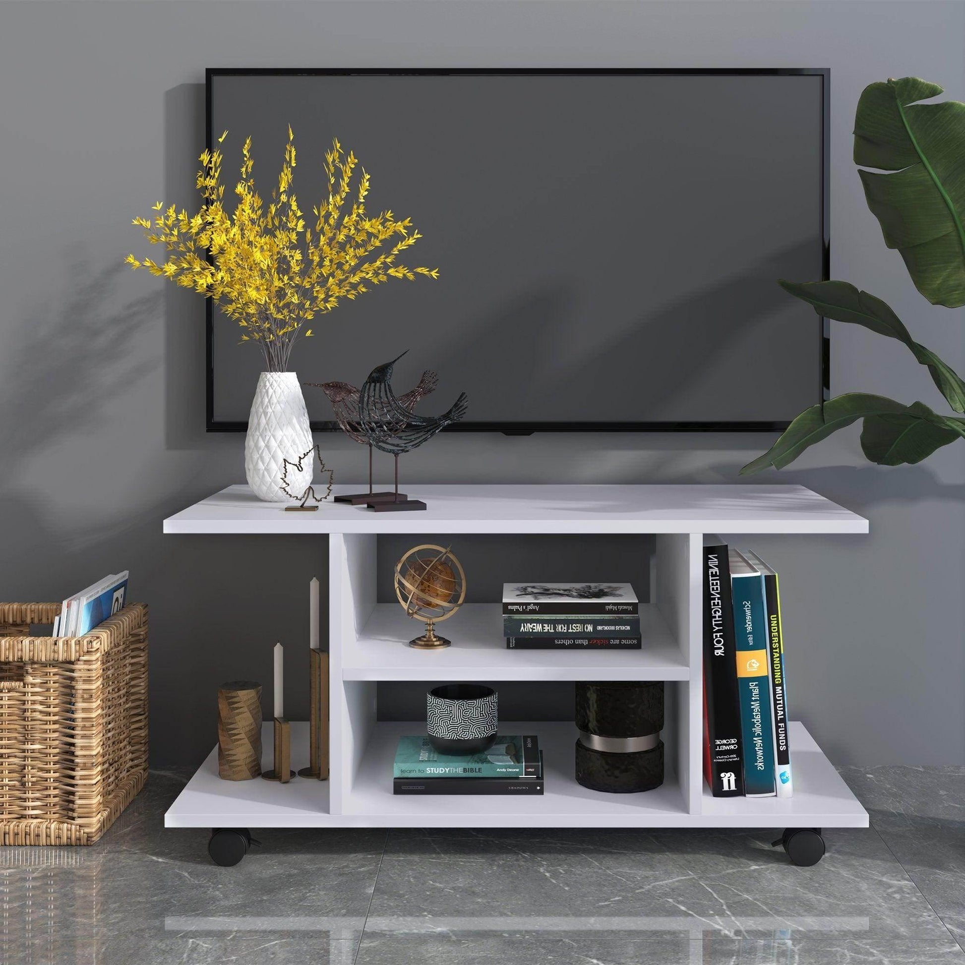 Modern white TV stand with shelves holding books, globe, decorative birds, vase with yellow flowers, and candles