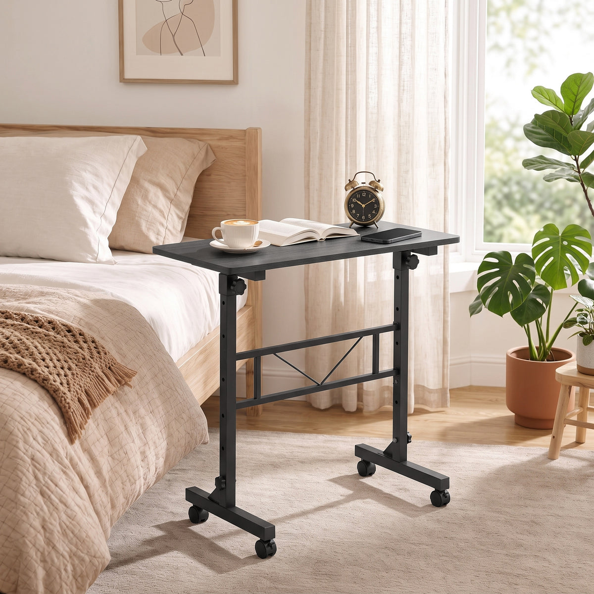 Adjustable overbed table beside bed with black top, metal frame, and rolling casters