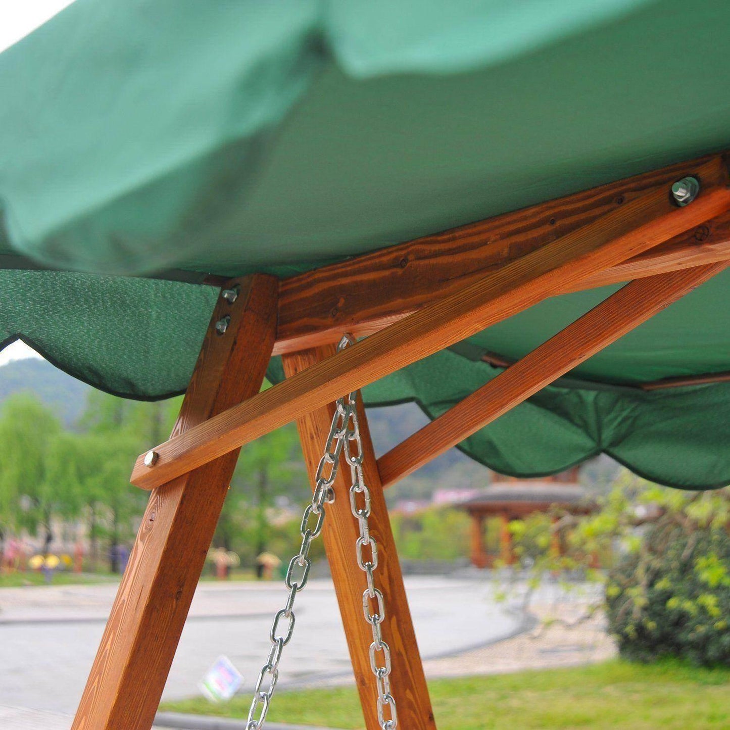 Close-up of wooden garden swing chair frame with green canopy and metal chain, outdoor setting