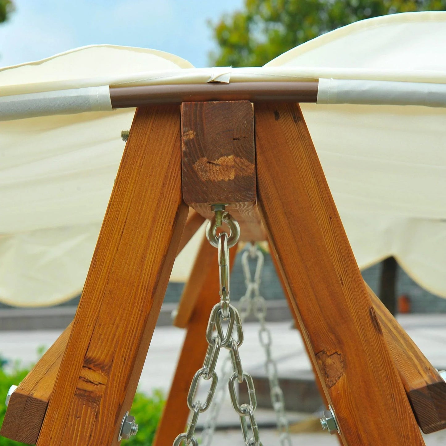 Close-up of wooden garden swing frame with metal chains and cream canopy, outdoor setting