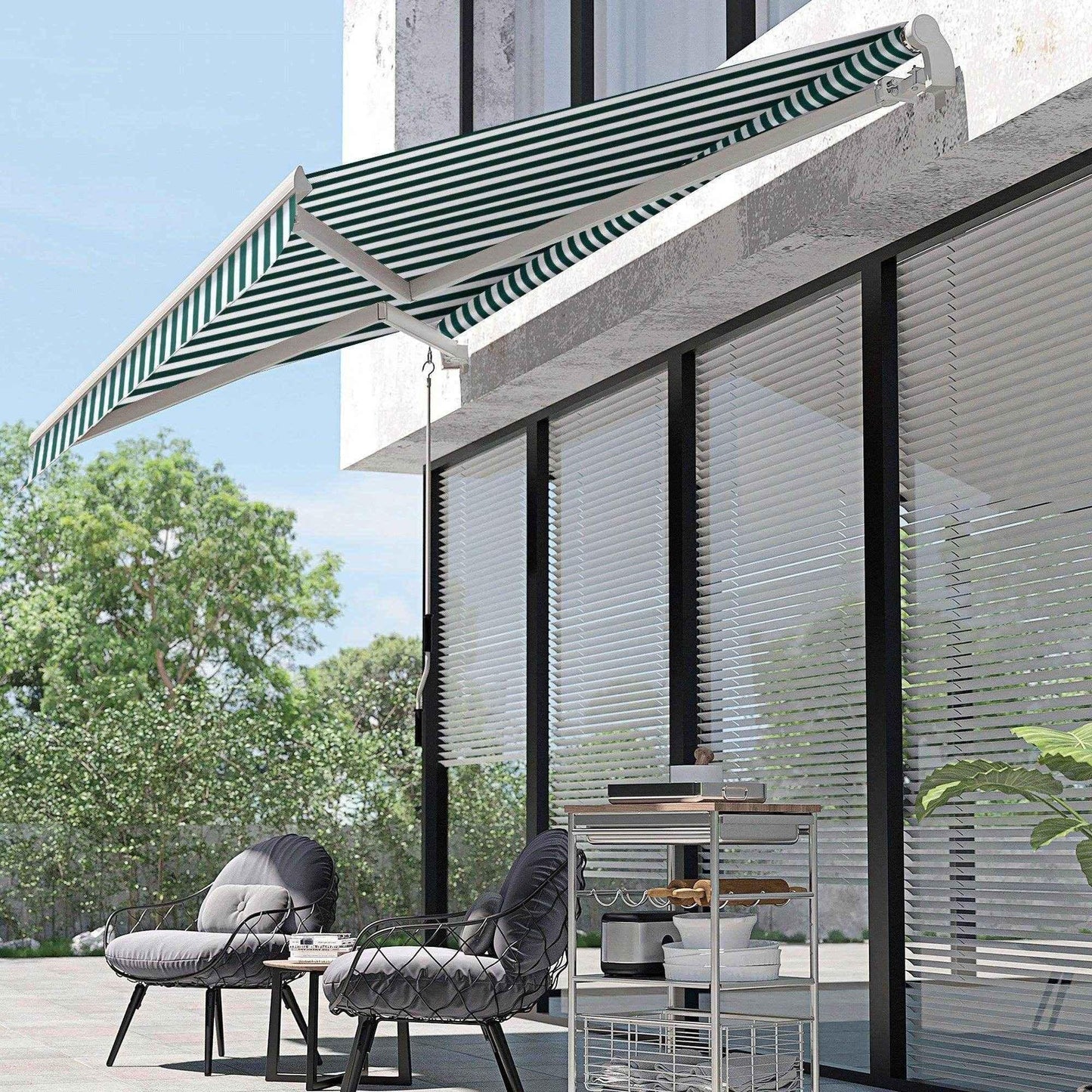 Green and white striped manual awning with winding handle installed above patio seating area with two cushioned chairs