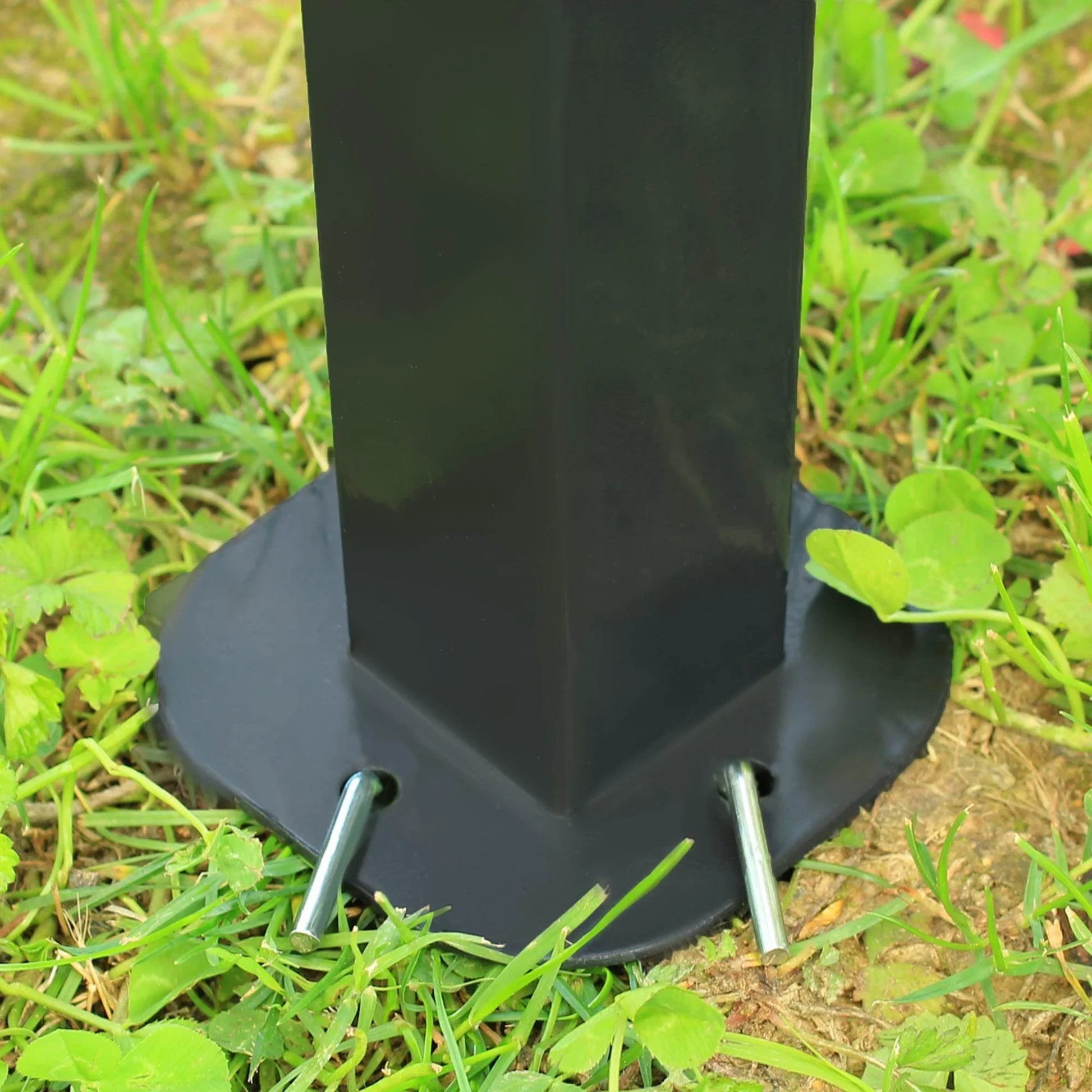 Close-up of black metal gazebo leg anchored with metal pegs on green grass outdoors