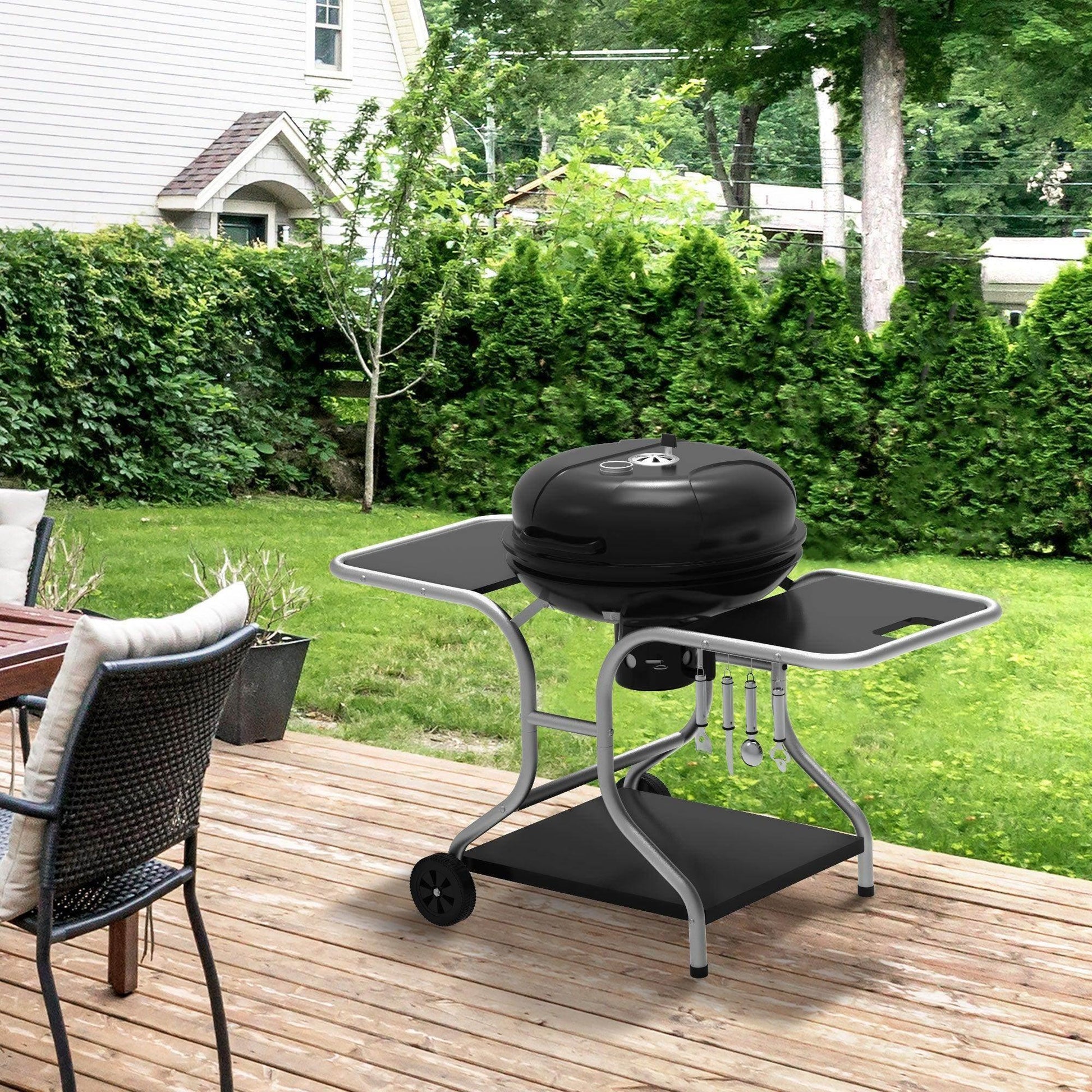 Outdoor charcoal grill trolley with wheels on wooden deck near patio furniture and green garden