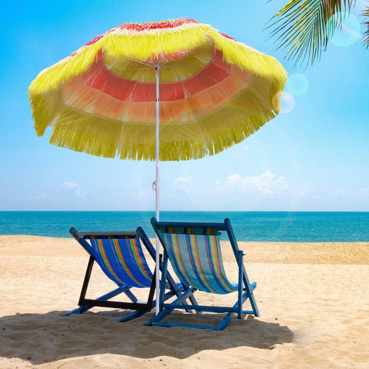 Colorful beach umbrella with fringe and two striped lounge chairs on sandy beach by blue sea