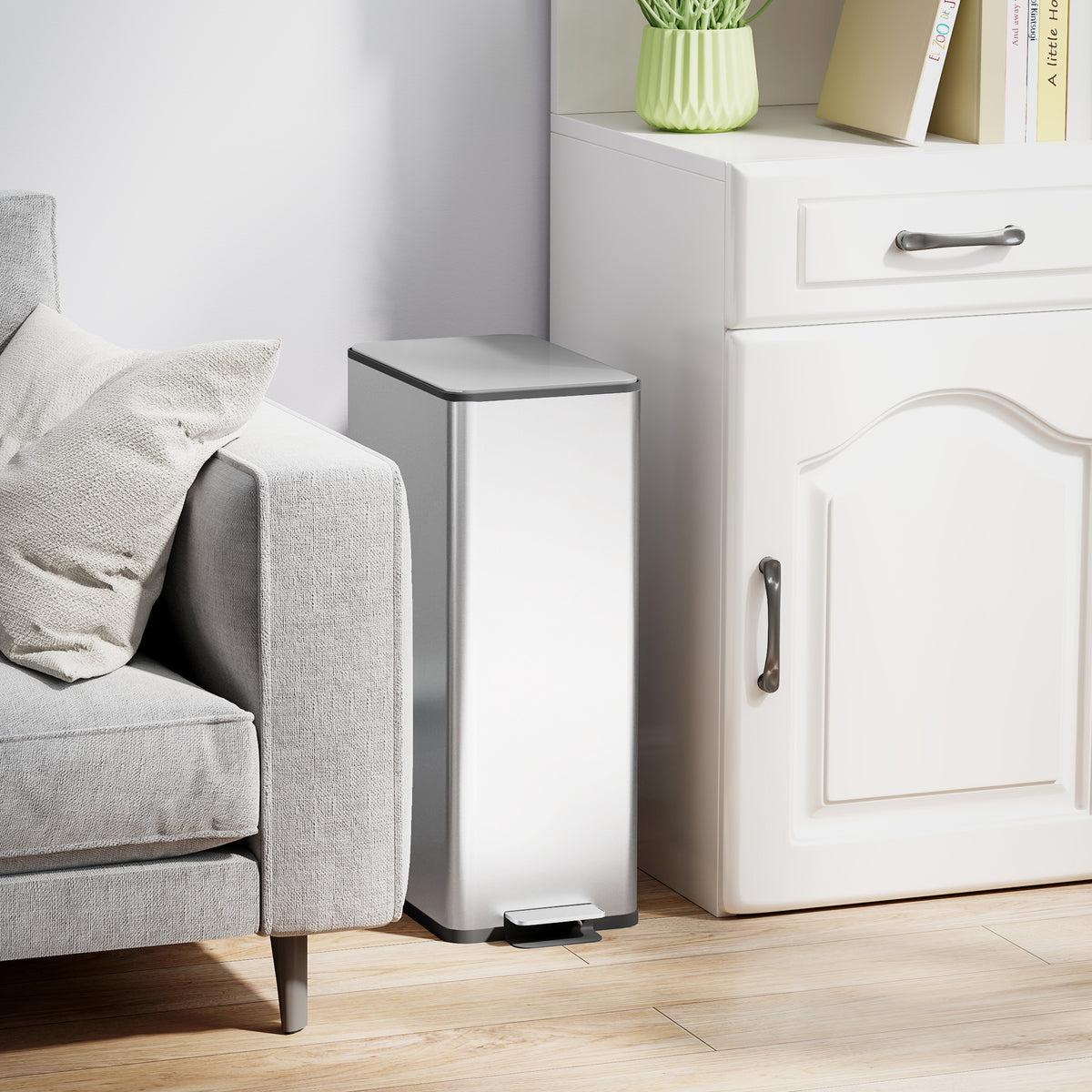 Stainless steel pedal bin beside furniture, with black lid and foot pedal