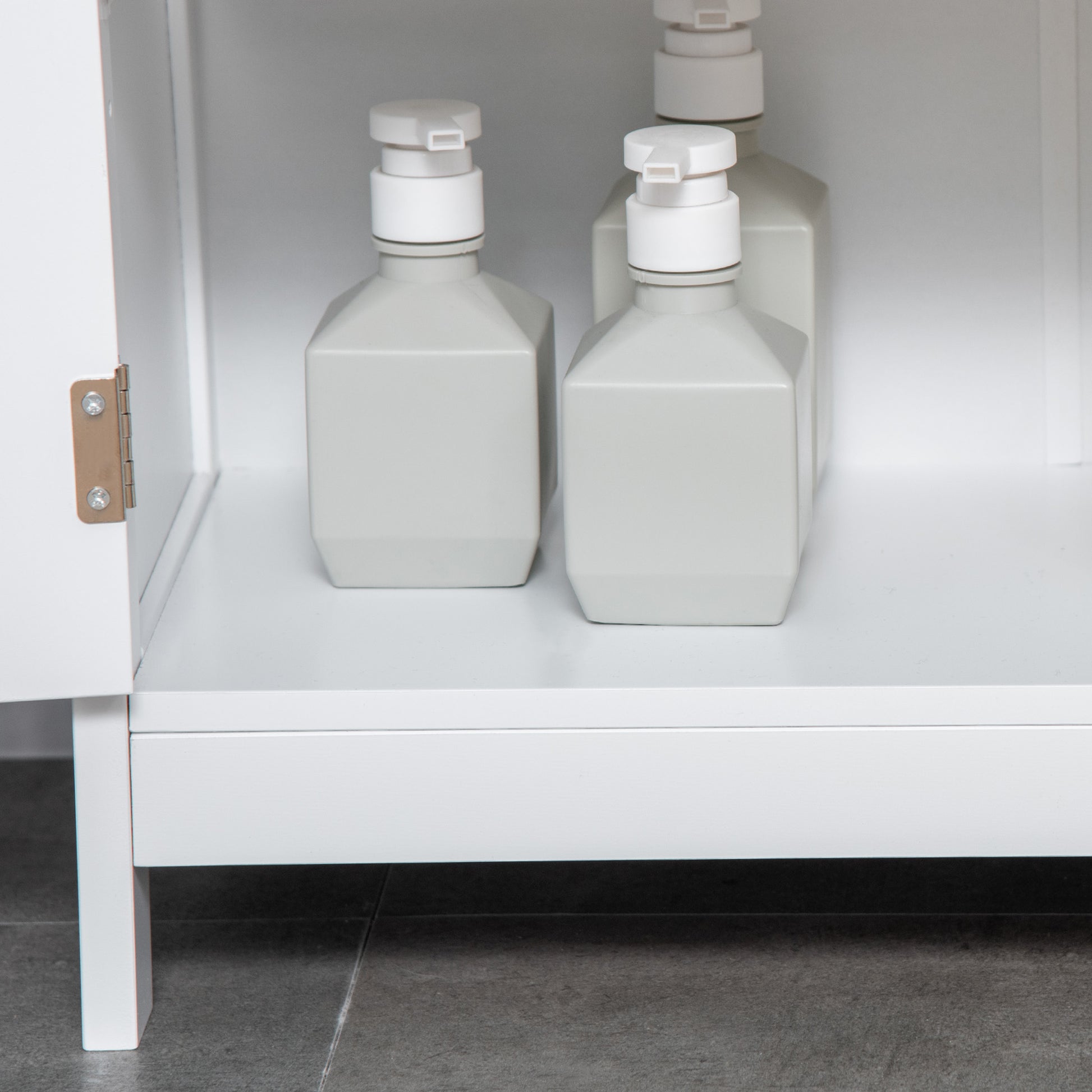 Set of white square soap dispensers stored in a modern bathroom cabinet on tiled floor