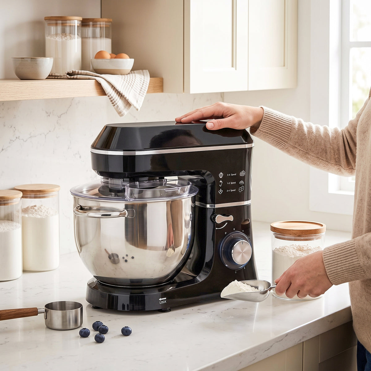 Black stand mixer with stainless bowl and splash guard, hand adjusting the mixing head