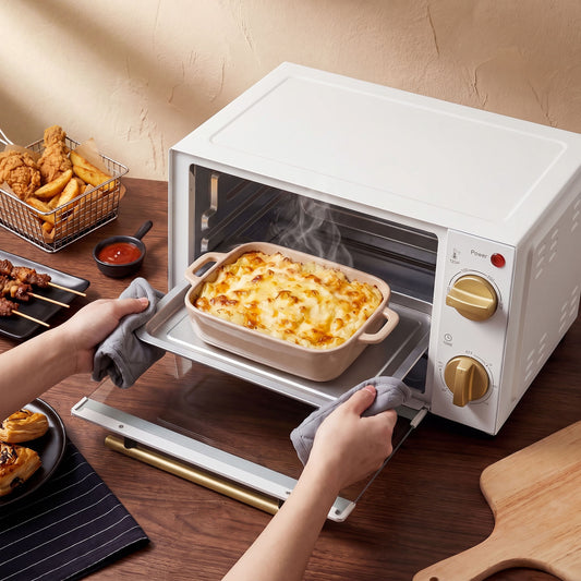 White mini toaster oven with open door, baking dish inside and front knob controls