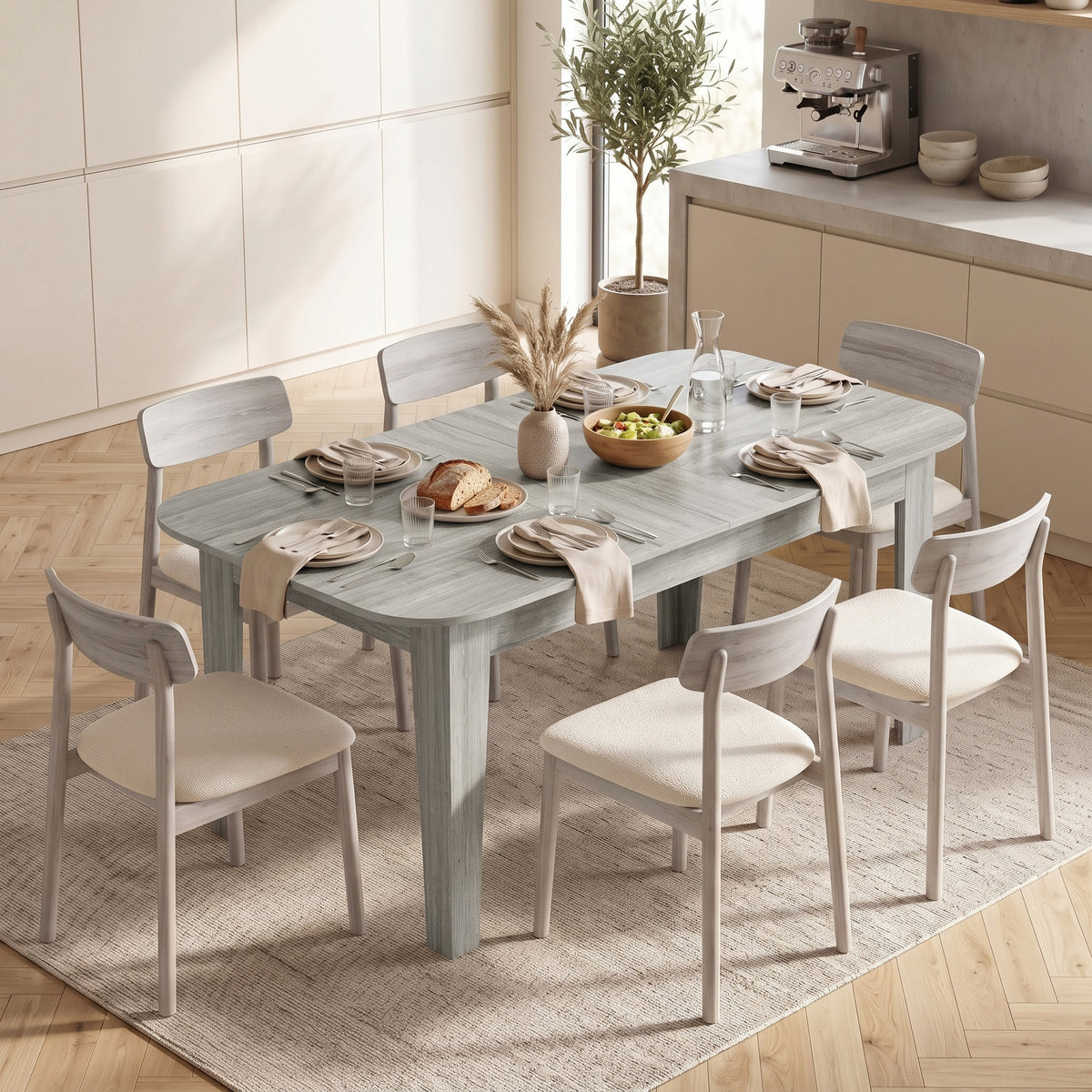 Grey wood-effect extendable oval dining table with extended leaf and dining chairs around it.