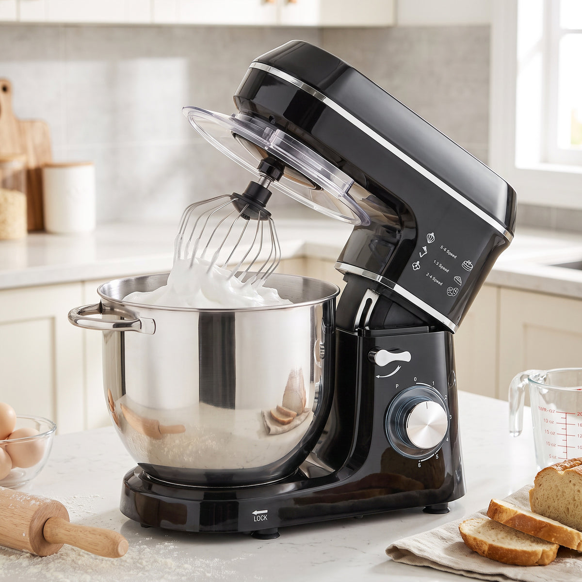 Black tilt-head stand mixer with clear splash guard and whisk attachment over stainless bowl