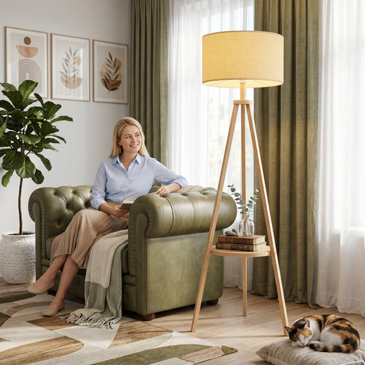 Tripod floor lamp with beige linen drum shade, wooden legs, and open storage shelf
