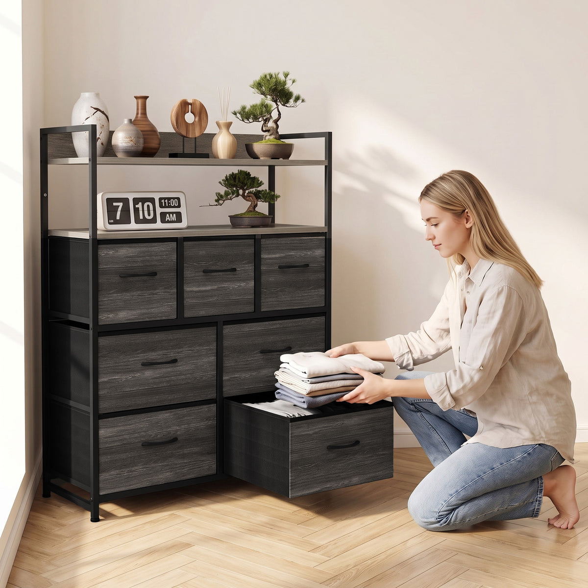 Grey wood-effect dresser with open shelves and seven drawers; person arranging folded items