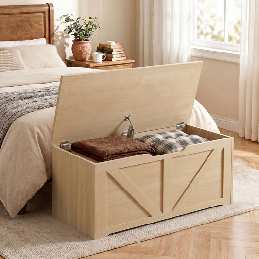 Light wood storage chest bench with open lid, holding folded bedding and a seat cushion