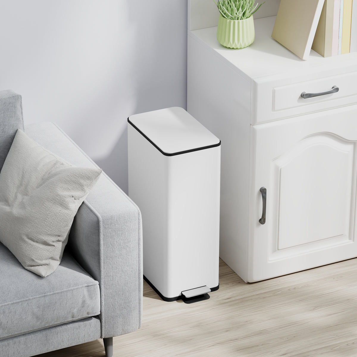 White slim pedal trash bin in a corner beside a sofa, black lid and base