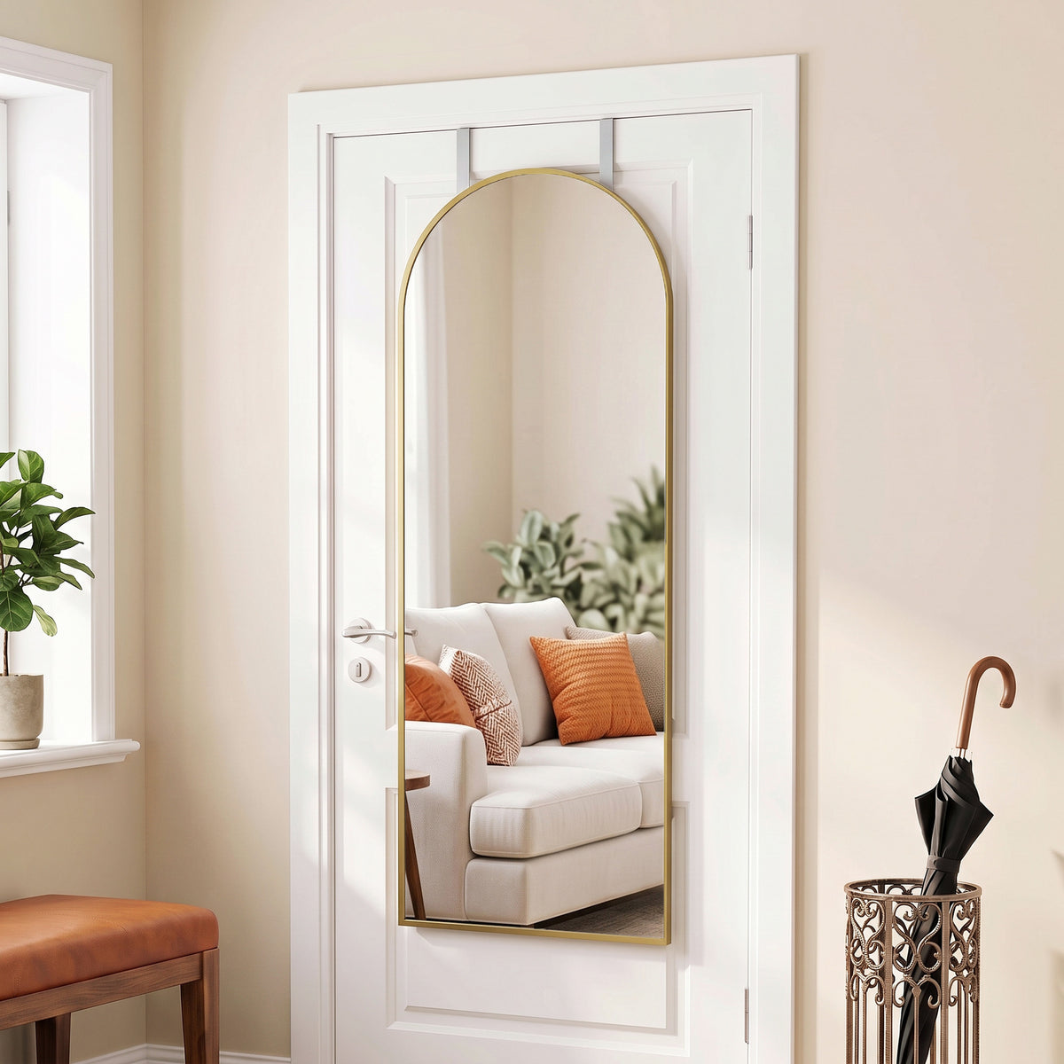Arched full-length hanging mirror with gold frame behind a white door