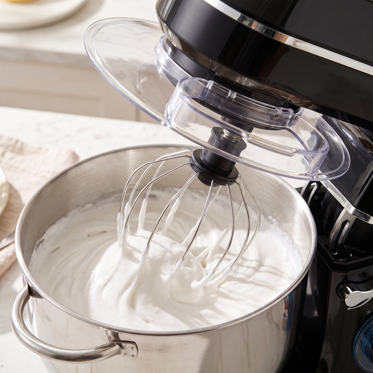 Whipped batter in stainless bowl with whisk attachment under clear splash guard