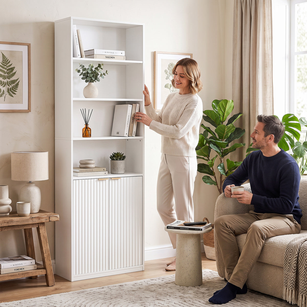 White tall bookcase with open shelves and double doors, person arranging items inside.